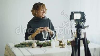 有魅力的、开朗的女人坐在餐桌前，在视频博客上录制关于相机上食物装饰设计的视频